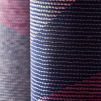 Close-up navy harlequin woven fabric with white dashed stripes, pink gradient edge and red accents.