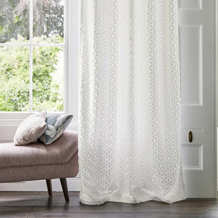 White sheer curtain with geometric lattice pattern, floor-length, light-filtering voile, in a bright living room with a pink chaise.