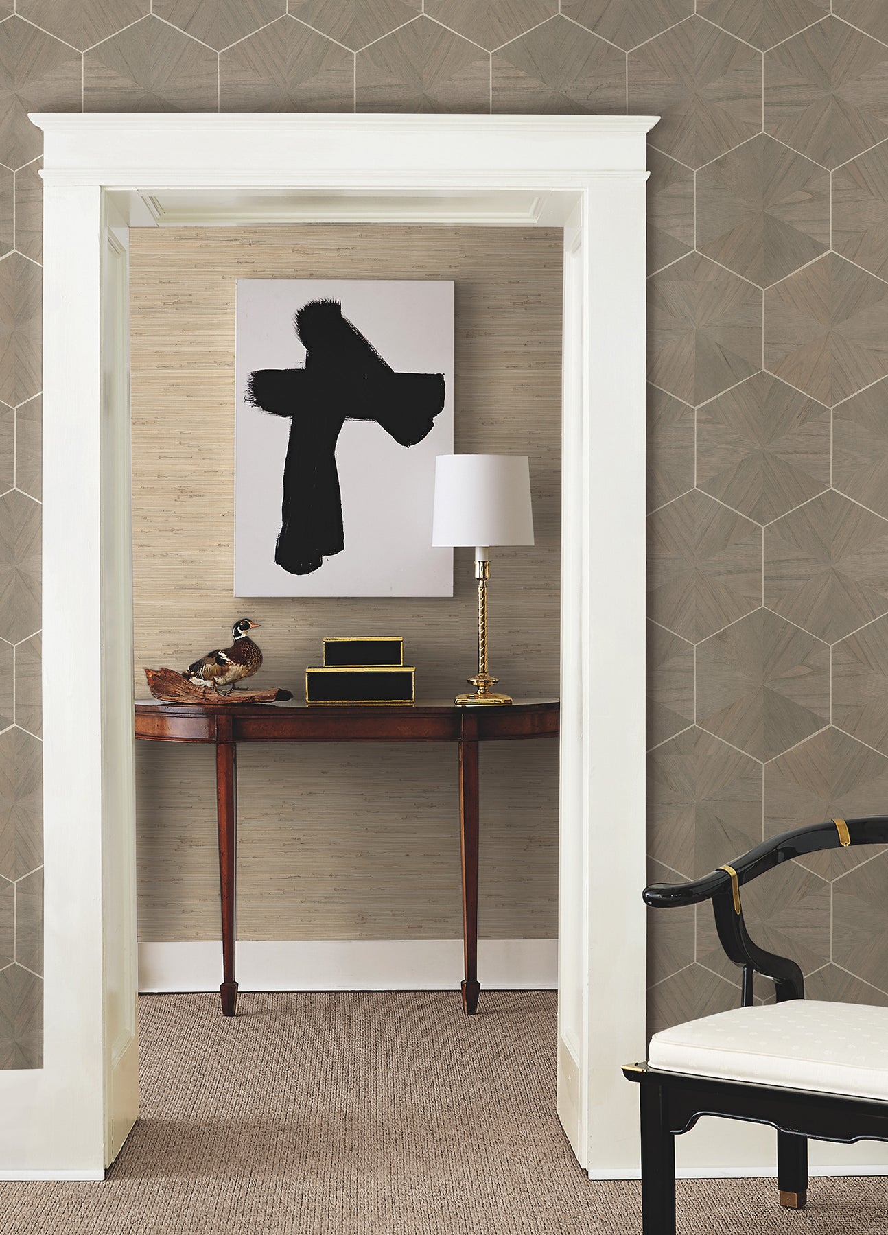 White doorway frames a hallway with a feature wall of brown wood-veneer wallpaper; it includes a wooden console, black abstract art, a brass lamp, and a ceramic bird statue.