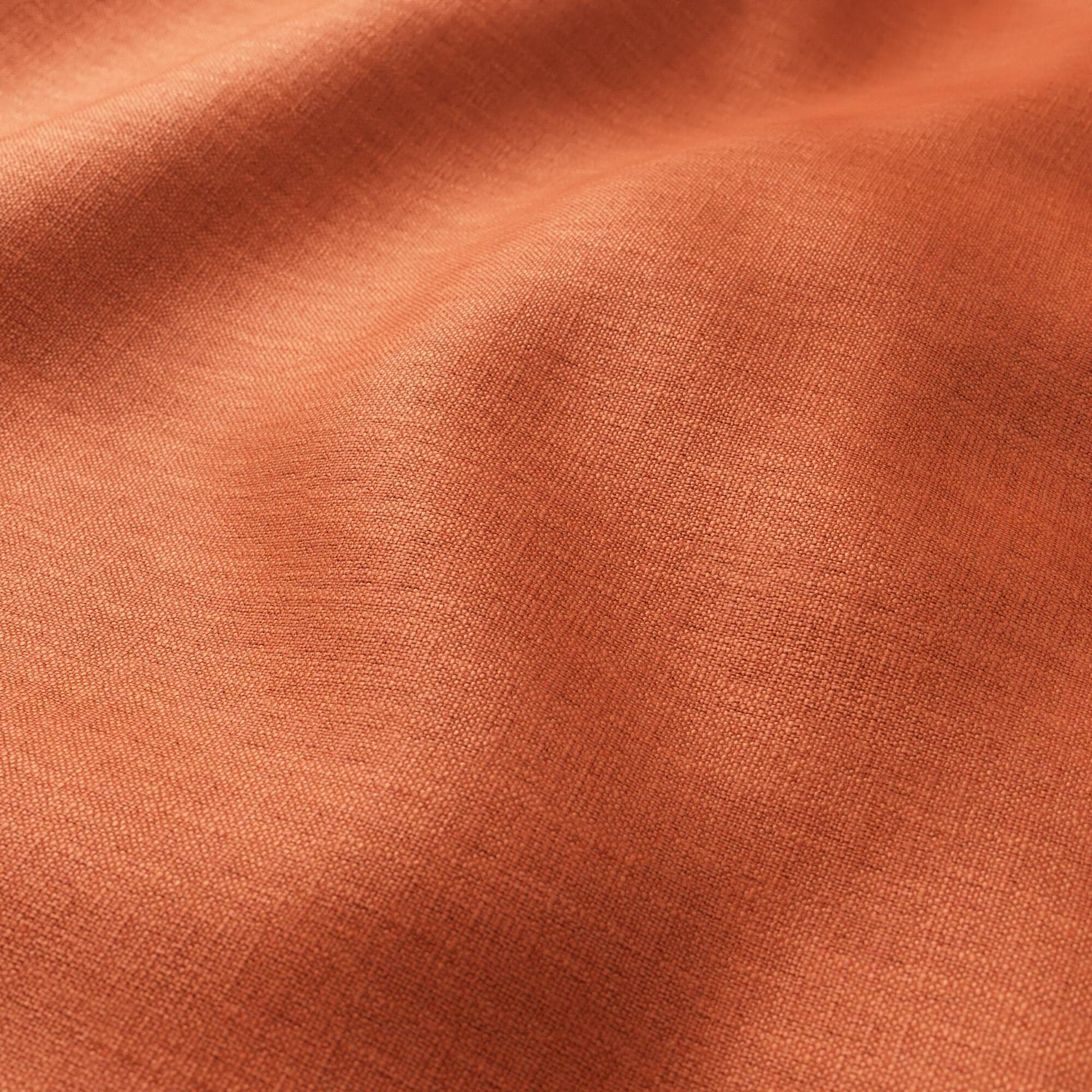 Close-up of warm orange terracotta woven fabric with fine texture and soft drape, casual apparel or home textiles.