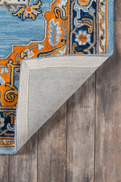 Blue ornate area rug with orange and light-blue border; woven texture, folded corner reveals beige backing on wood floor.