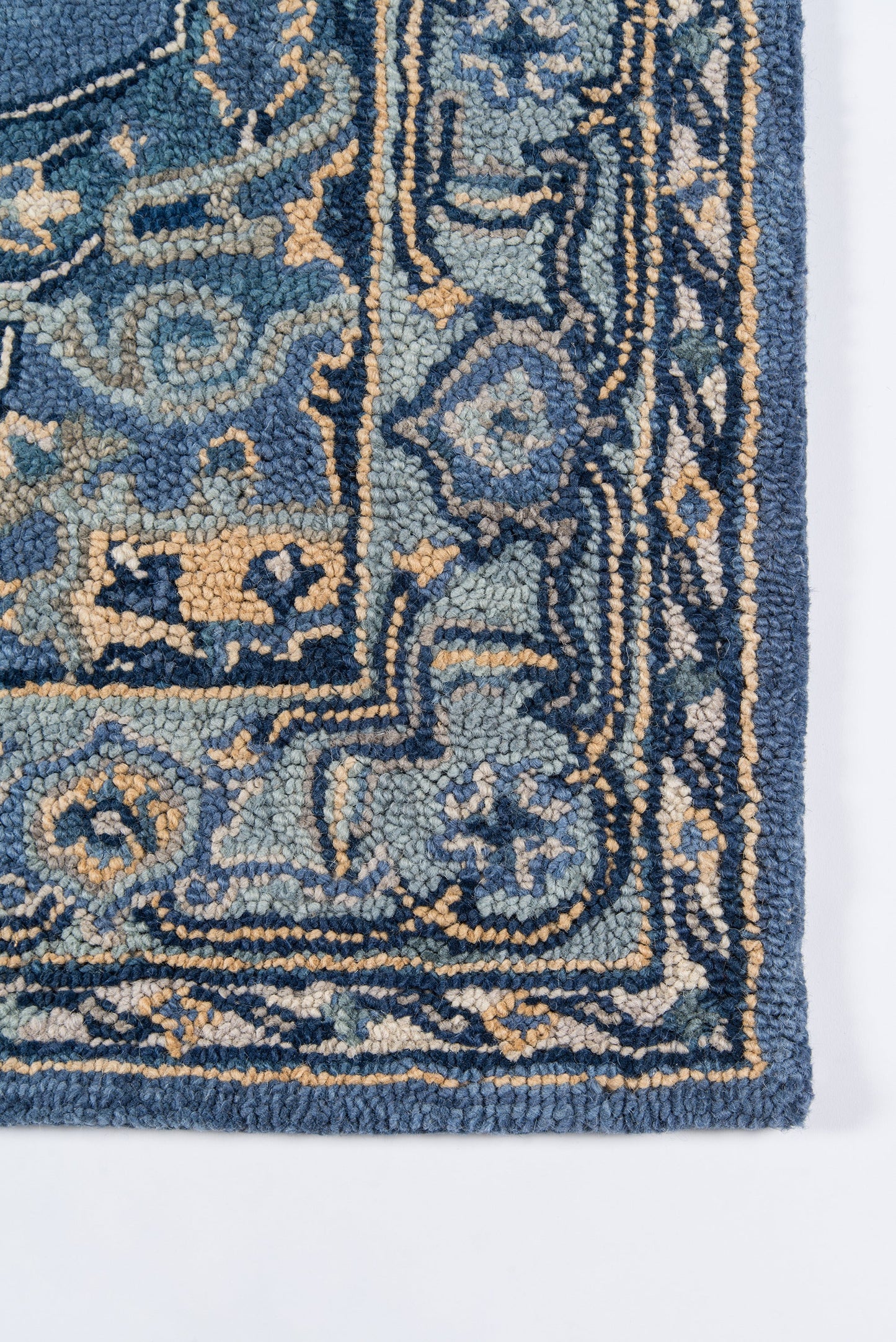 Close-up of a blue ornate tufted rug corner with teal and beige motifs and decorative border.