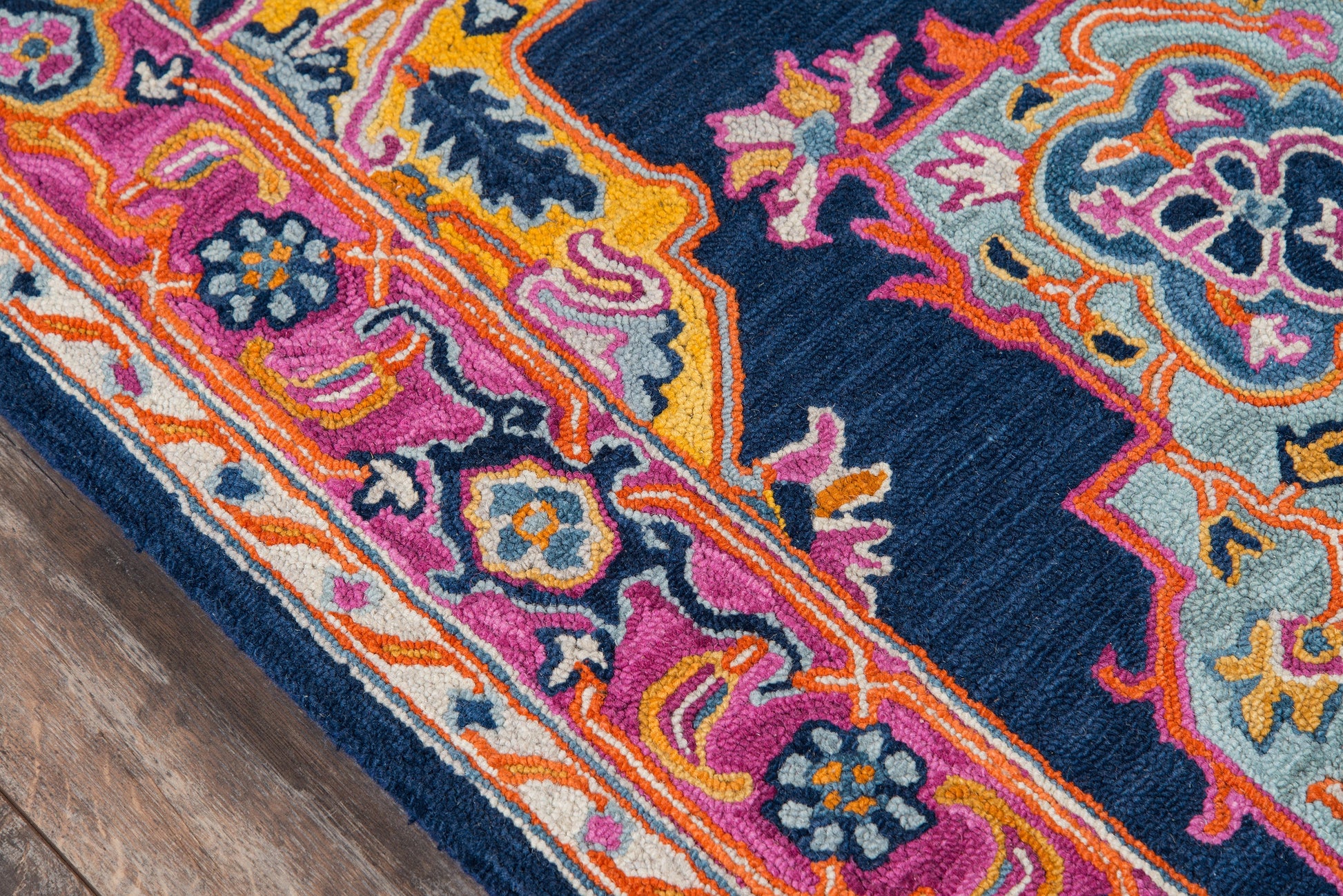 Ibiza-style rug with navy field, vivid pink, orange and turquoise florals and ornate border, on wood floor.