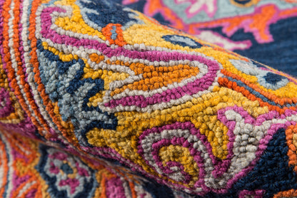 Close-up of a vibrant tufted rug with pink, orange, yellow and navy geometric patterns; boho Ibiza style.