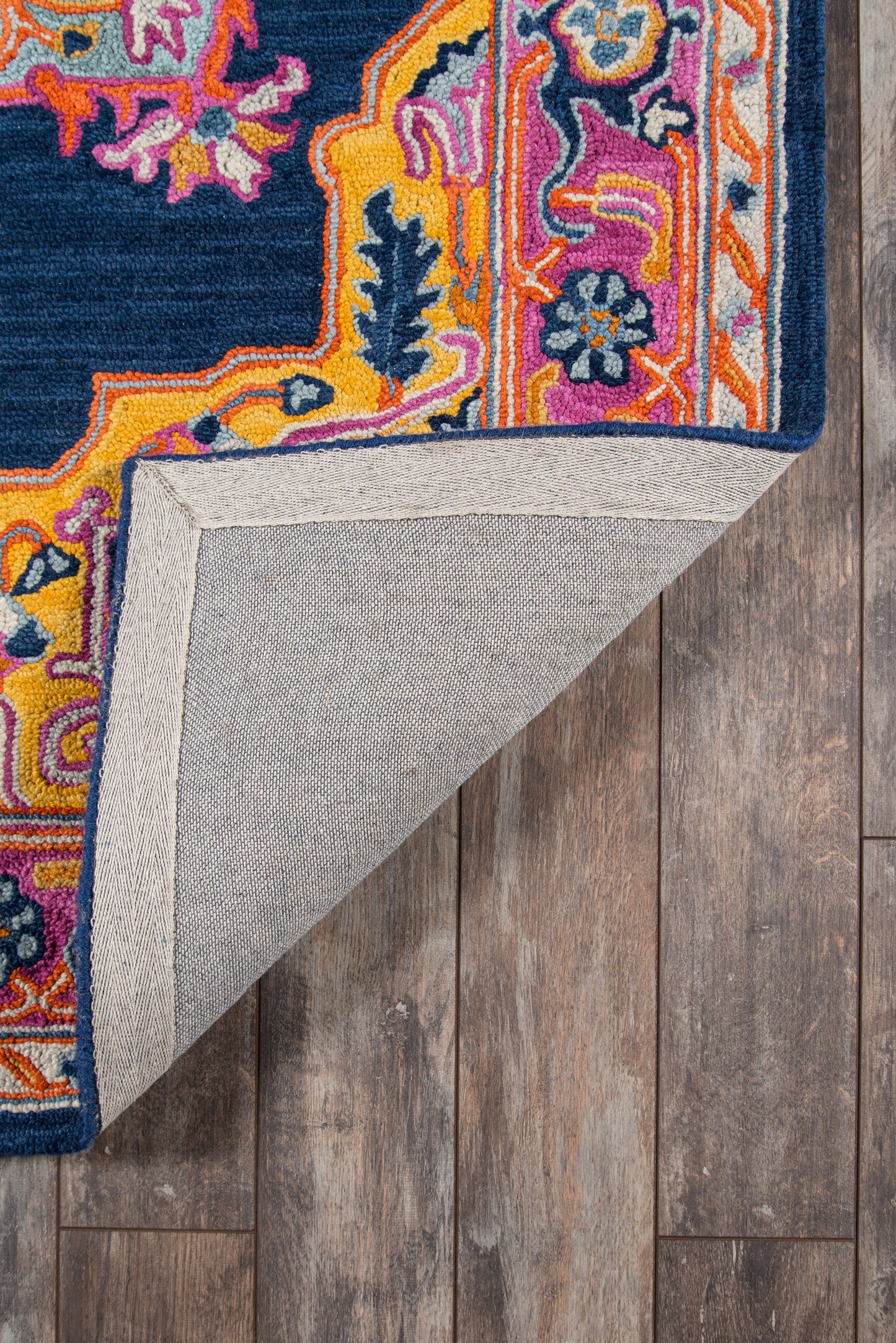 Vibrant oriental-style rug with navy field and bright pink, orange, yellow border; folded corner shows pale gray backing.