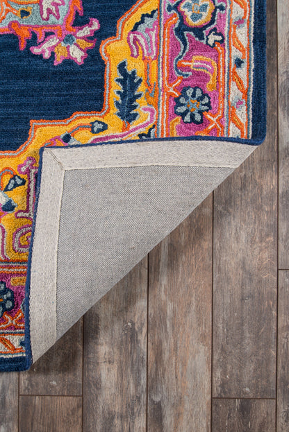 Colorful ornate rug with a navy center and vibrant multicolor floral border; folded corner shows grey backing on wood floor.