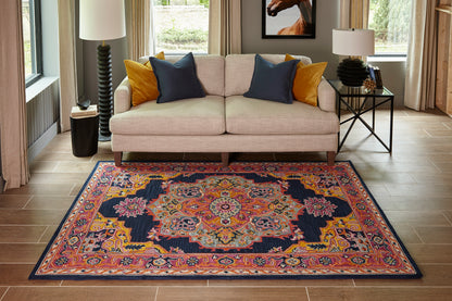 Beige sofa with navy and mustard cushions, colorful oriental rug in navy, pink, orange; wood floors, side tables with lamps.