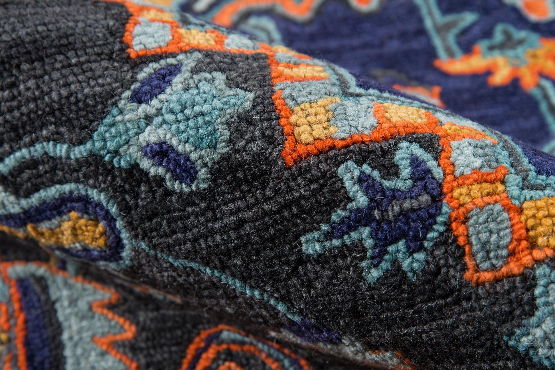 Close-up of a plush woven rug with blue, teal, orange & yellow geometric patterns on a dark navy background