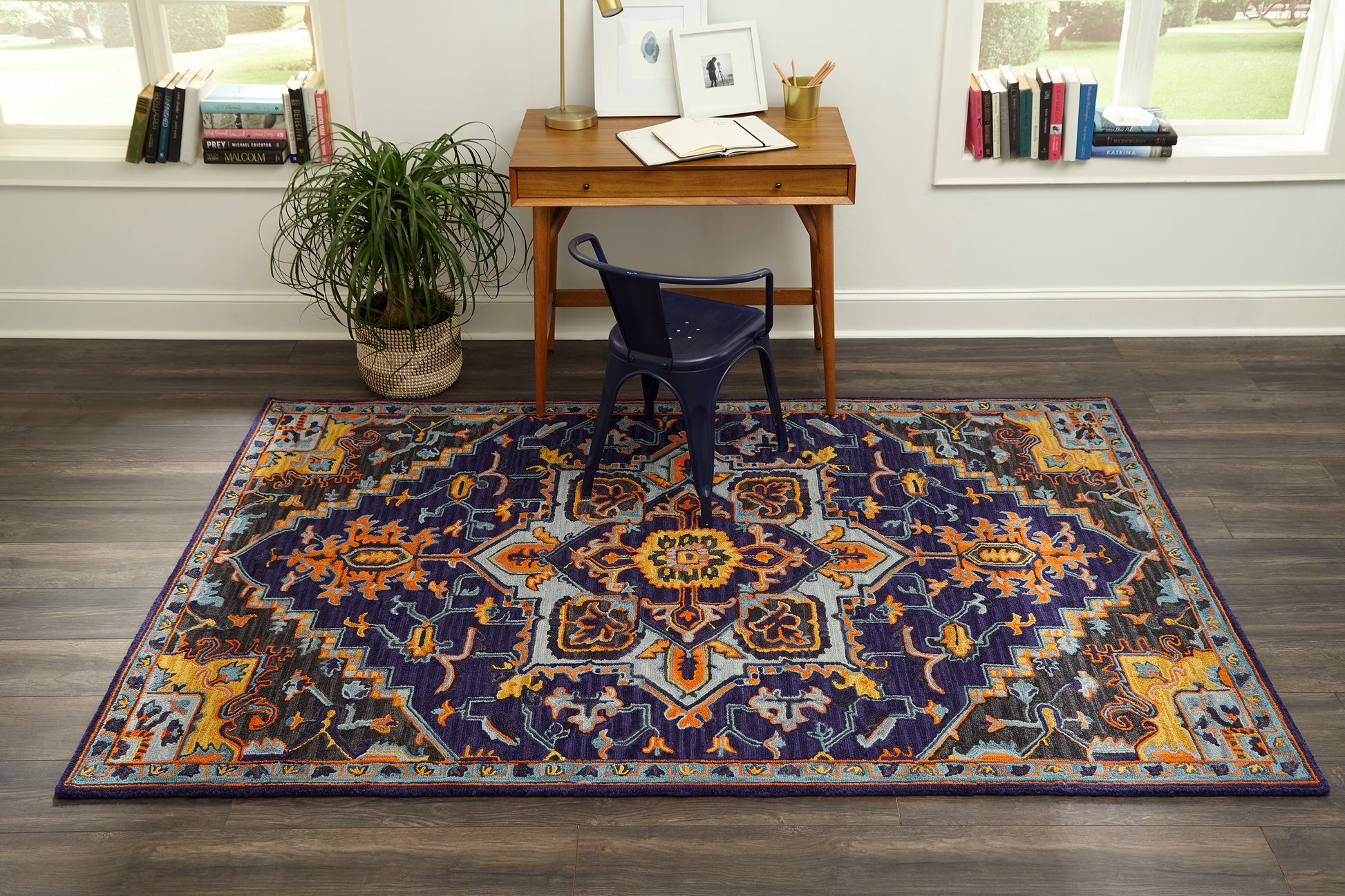 Rectangular oriental rug with navy field and orange, cream, and light-blue medallions under a wooden desk.