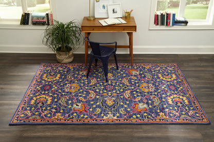 Blue oriental rug with multicolor floral motifs and orange border in a home office with a wooden desk and navy chair.