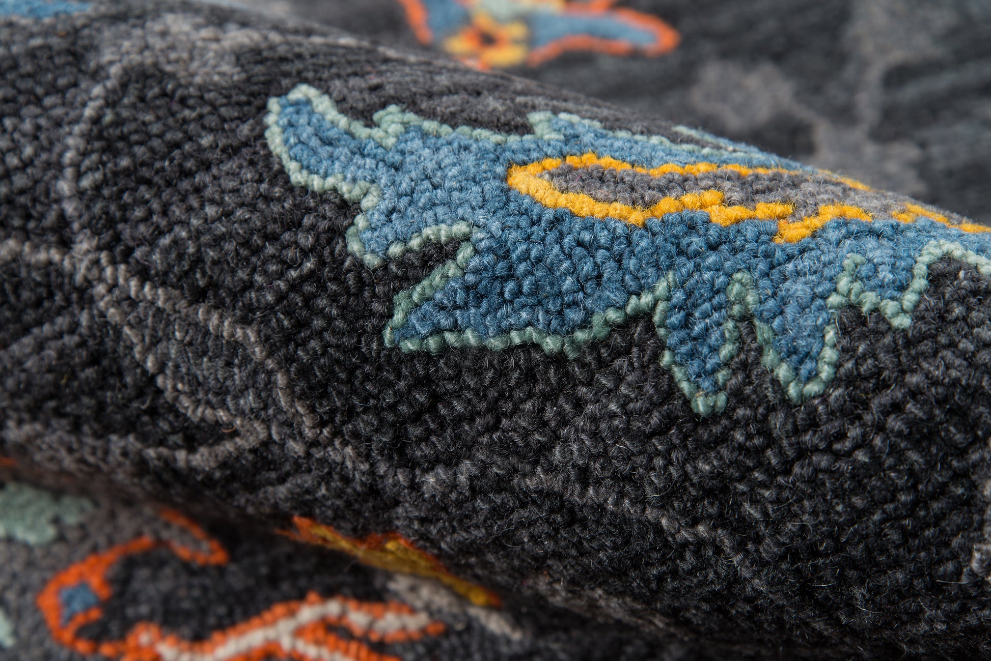 Dark plush rug with blue turquoise leaf embroidery outlined in pale green and orange accents.