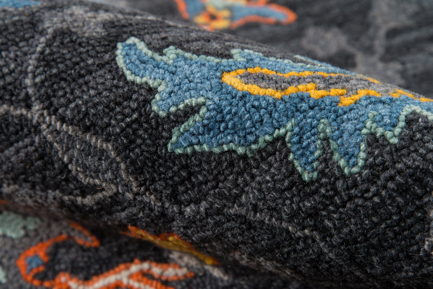 Close-up of black textured runner rug with a blue leaf-shaped motif, teal edging & orange-yellow trim.
