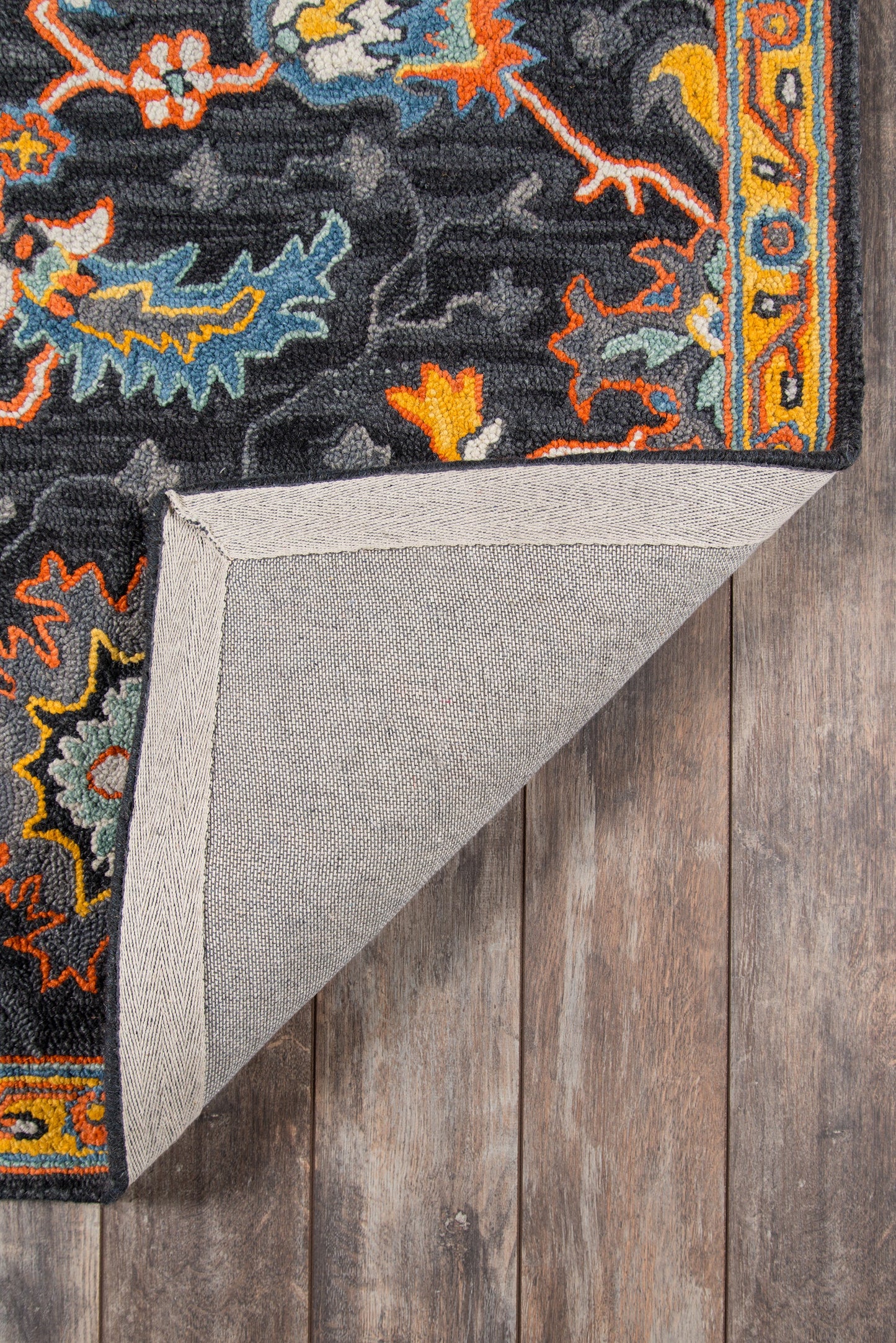 Ibiza-style oriental rug with black field, orange, blue, teal and yellow floral motifs; bordered edge; folded corner reveals grey backing.