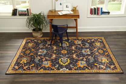 Dark gray oriental rug with vibrant orange, blue and yellow floral medallions; yellow border under a wooden desk and blue chair.