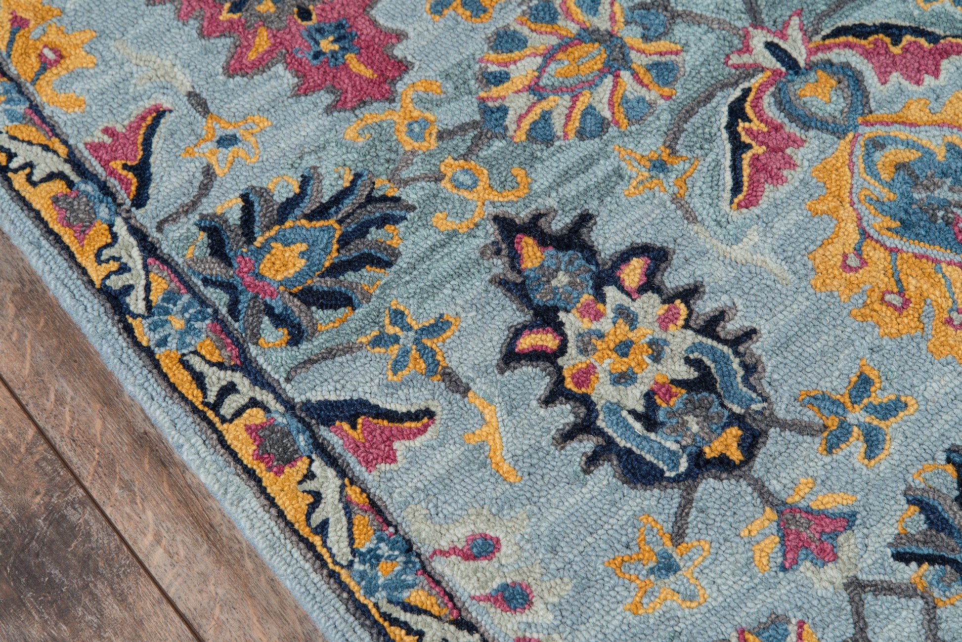 Blue patterned runner rug with yellow, orange and pink floral motifs, navy border, folded corner on wooden floor.