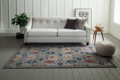 Blue floral area rug with yellow and red accents, 5' x 8', with a knitted pouf and wooden side table nearby.