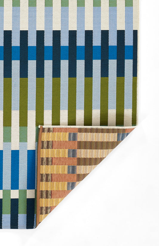 Woven rug 2' x 3' with vertical stripes in blue, teal, olive and cream; folded corner reveals a warm mustard-brown reverse.