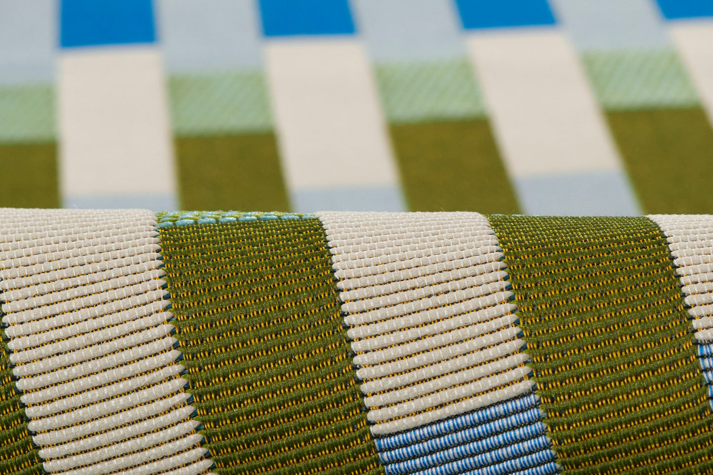 Close-up of striped woven rug fabric in olive green, beige & blue hues.