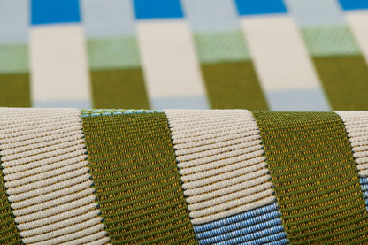 Close-up of striped woven rug fabric in olive green, beige & blue hues.