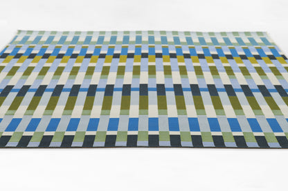 Rectangular woven rug with a modern geometric grid of blue, green and yellow stripes.
