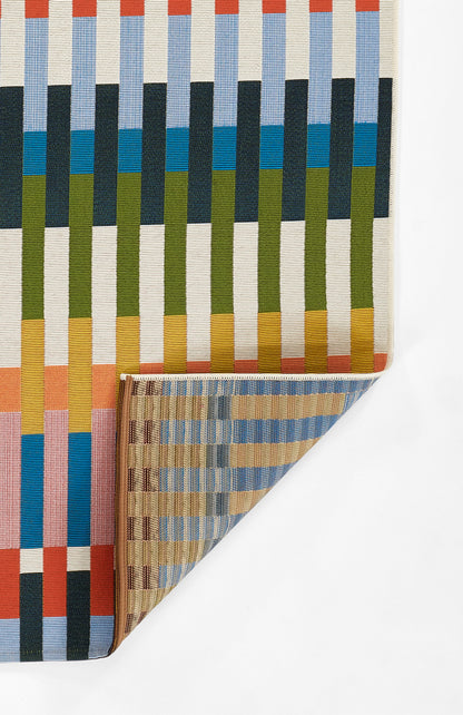 Rectangular striped woven rug with vertical ribbons in blue, green, yellow, orange; folded corner reveals tan underside.