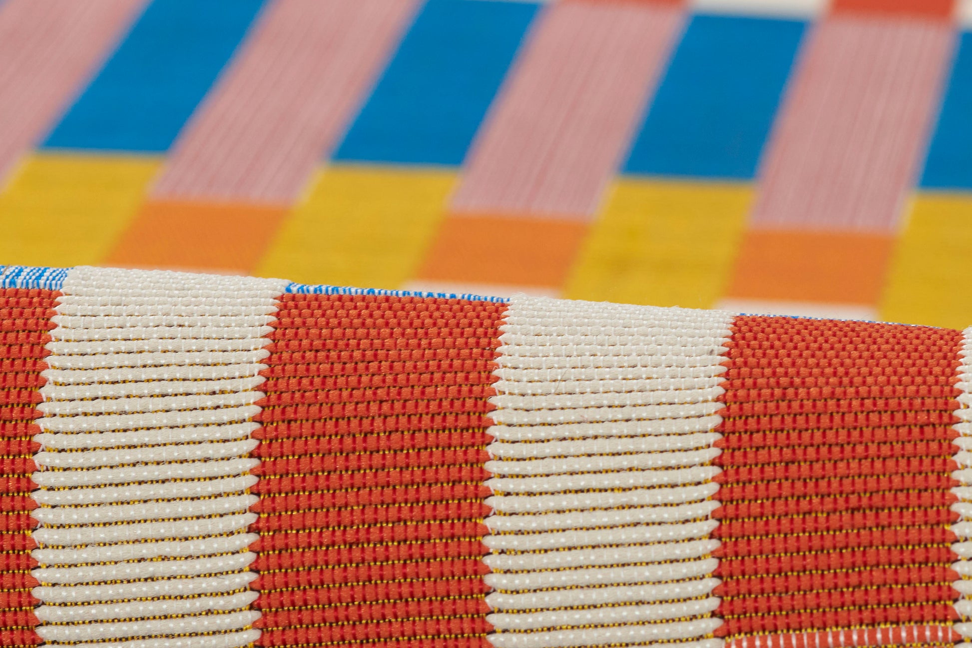 Close-up of a red and white striped woven rug with a colorful blue, yellow and orange block backdrop.