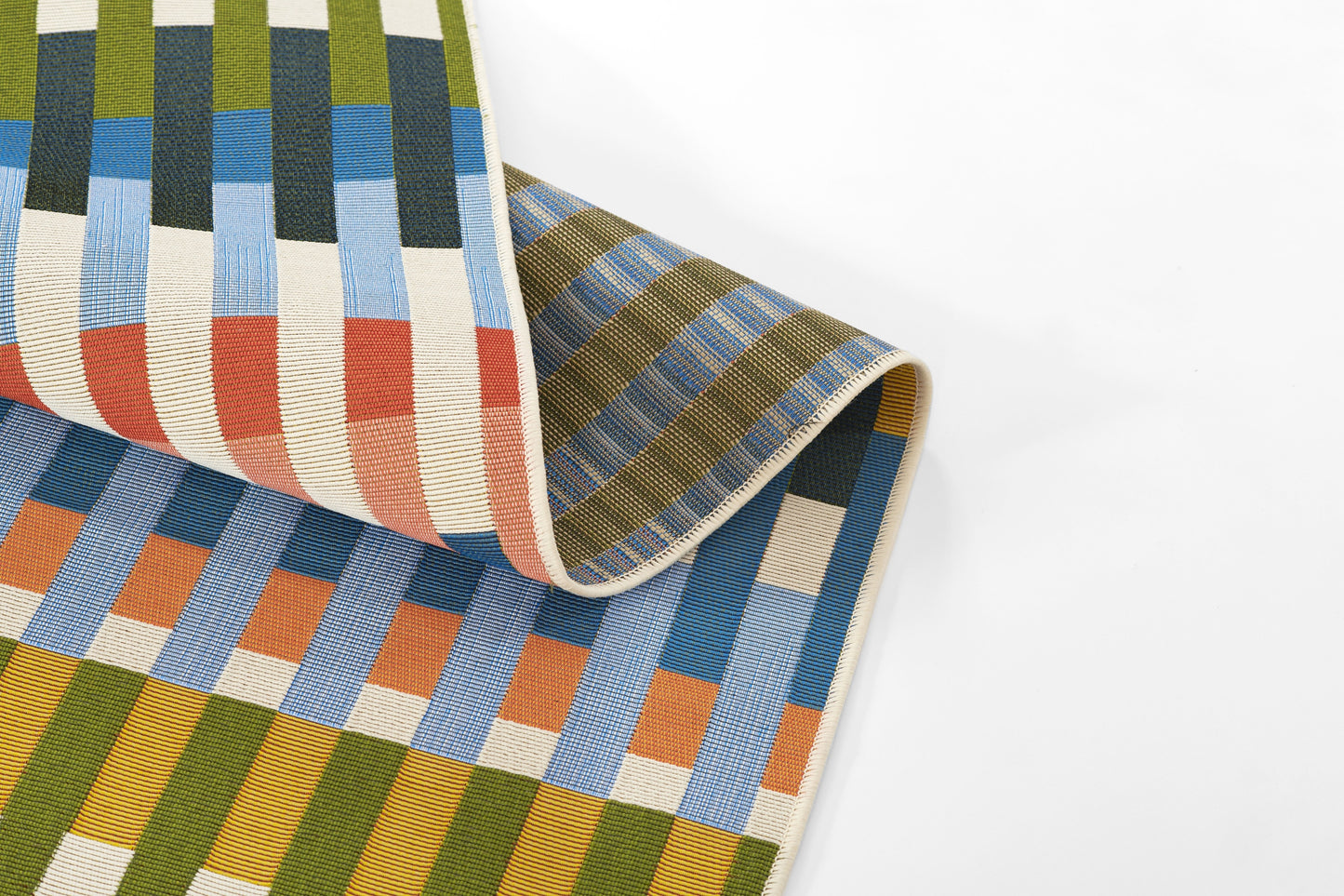 Colorful woven rug with multicolored vertical striped blocks in olive, blue, orange, cream; folded edge visible.