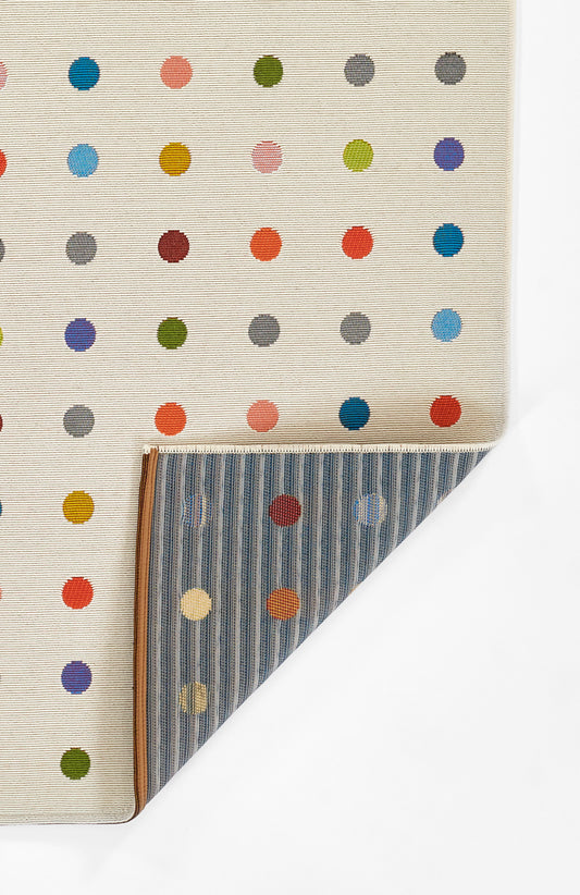 Beige rug with multicolor polka dots; folded to reveal blue striped reverse and brown trim, decorative textile.