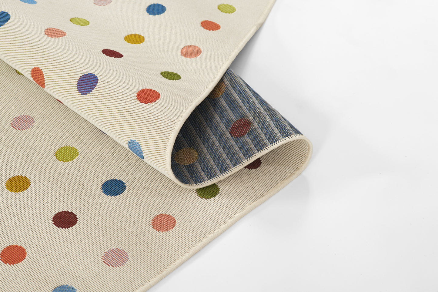 Beige woven rug with multicolor polka dots, rolled to show blue striped underside and stitched cream edge.