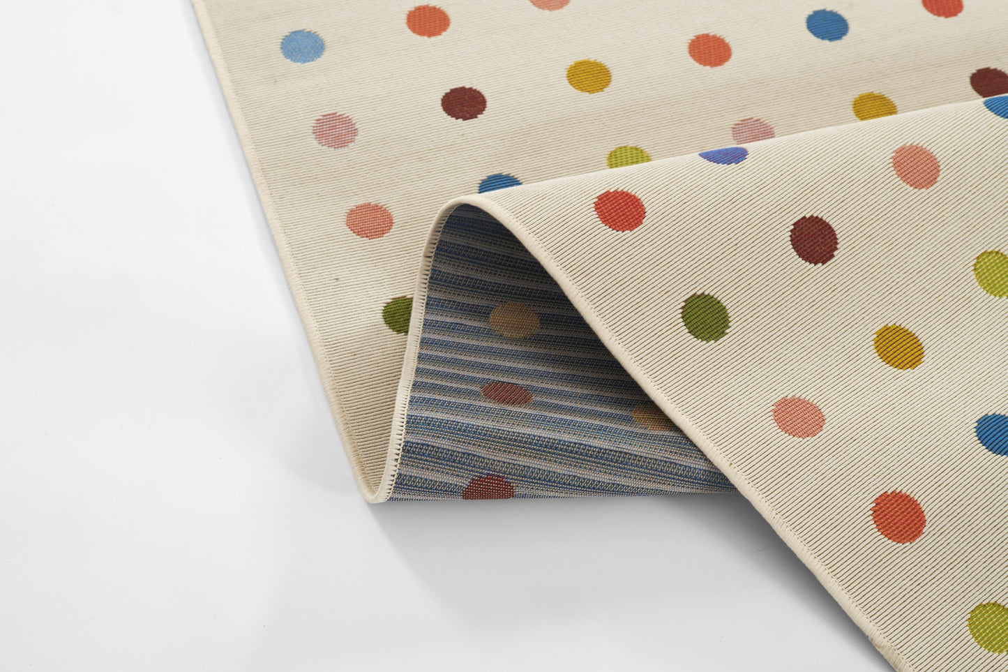 Cream rug with multicolored polka dots; rolled corner reveals blue striped underside.