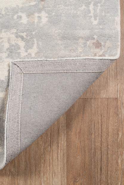 Grey and beige patterned area rug with plush pile; rolled corner shows light gray herringbone backing on wood floor.