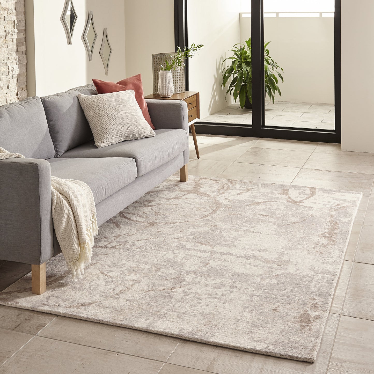 Plush beige patterned area rug under a light gray sofa with wooden legs and a cream throw.
