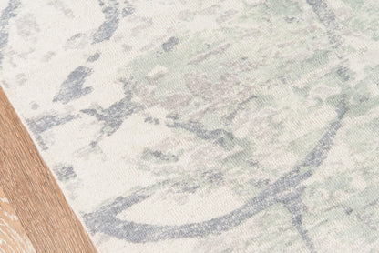 Gray flat-weave rug with pale sage-green and blue-gray abstract motifs on a light background, on a wooden floor.