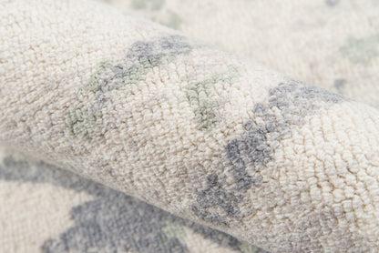 Beige textured rug with soft loop pile and muted gray green geometric patterns.