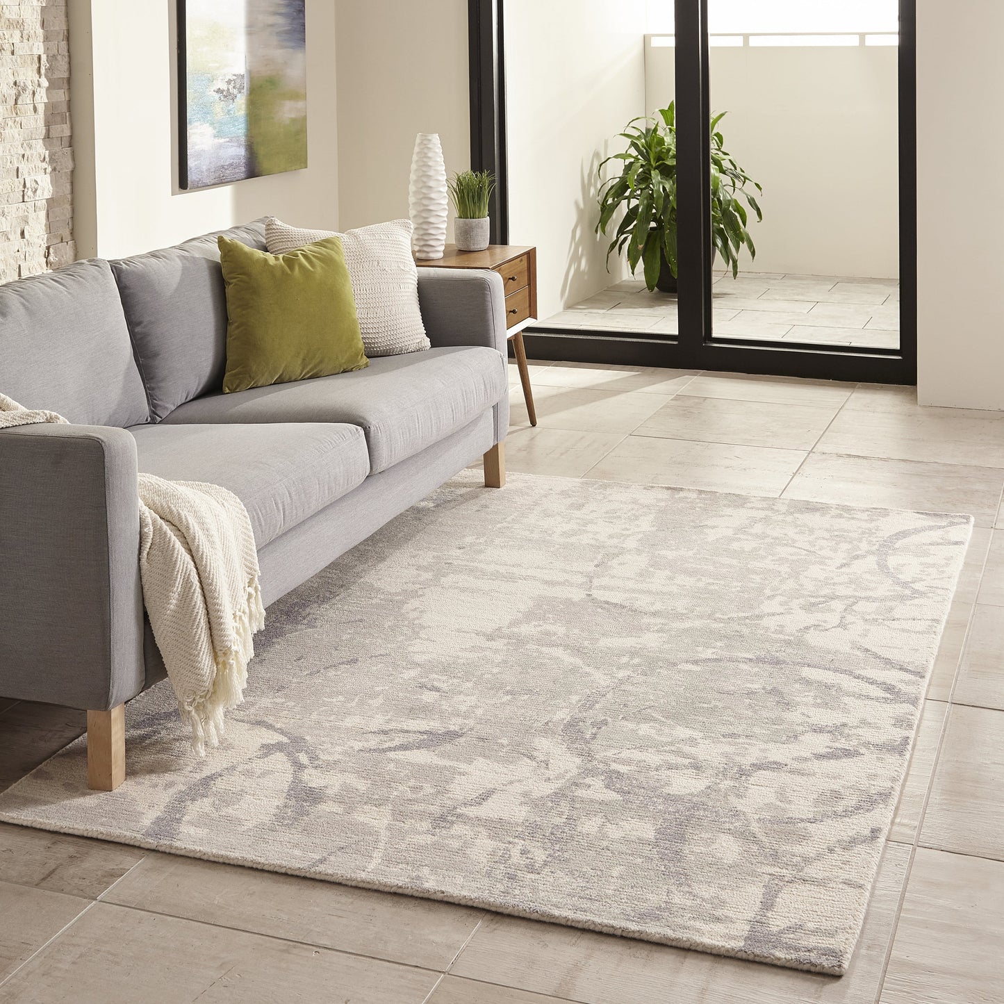 Light gray abstract-pattern area rug under a modern gray sofa with olive-green cushion in a bright living room.