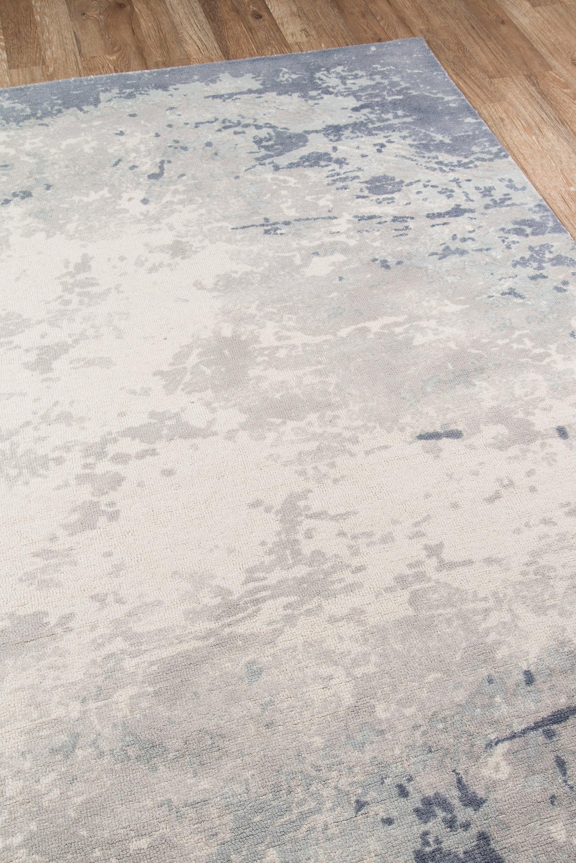Rectangular area rug in pale cream with blue distressed abstract pattern on wood floor.