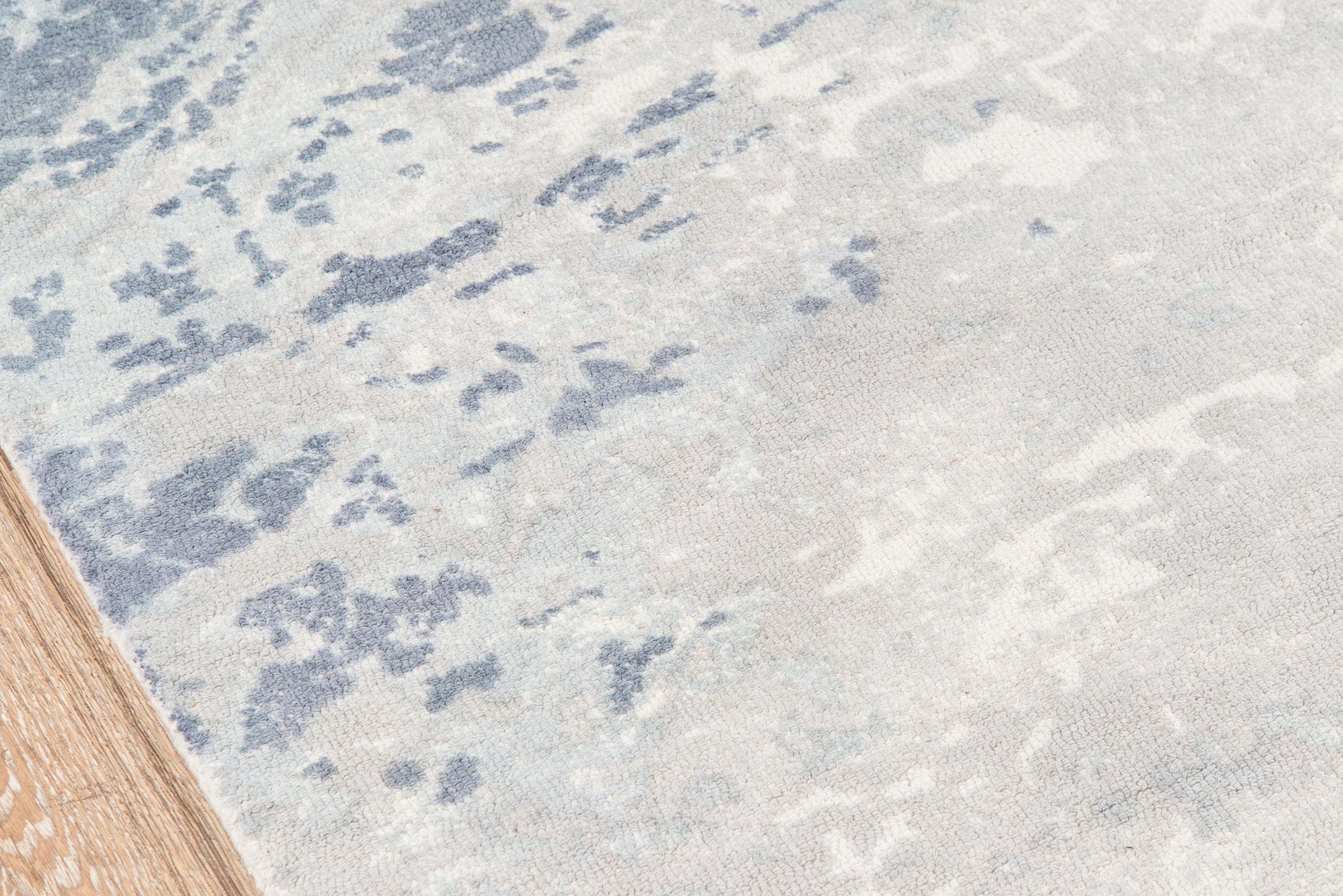 Blue & ivory abstract patterned rug with wood floor edge.