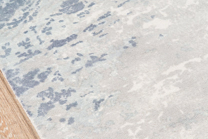 Blue & ivory abstract patterned rug with wood floor edge.