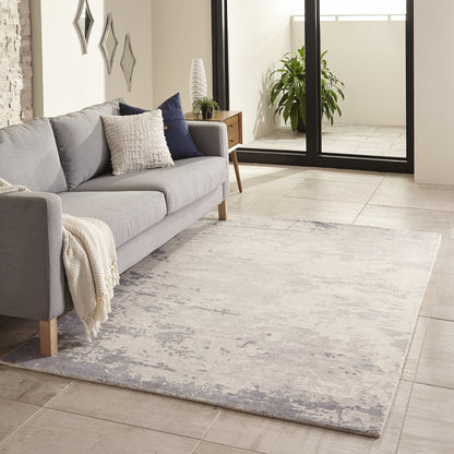Light gray modern sofa with navy cushions and a cream throw on a pale blue-gray distressed rug in a bright living room.