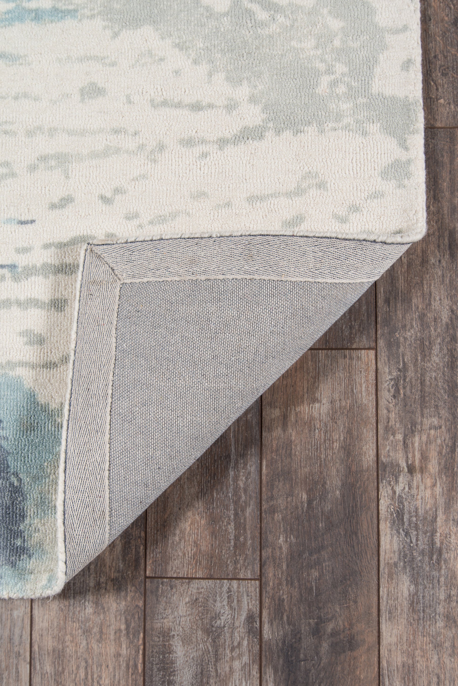 Cream and blue abstract area rug with teal accents, grey underside, herringbone-edge binding on wood floor.
