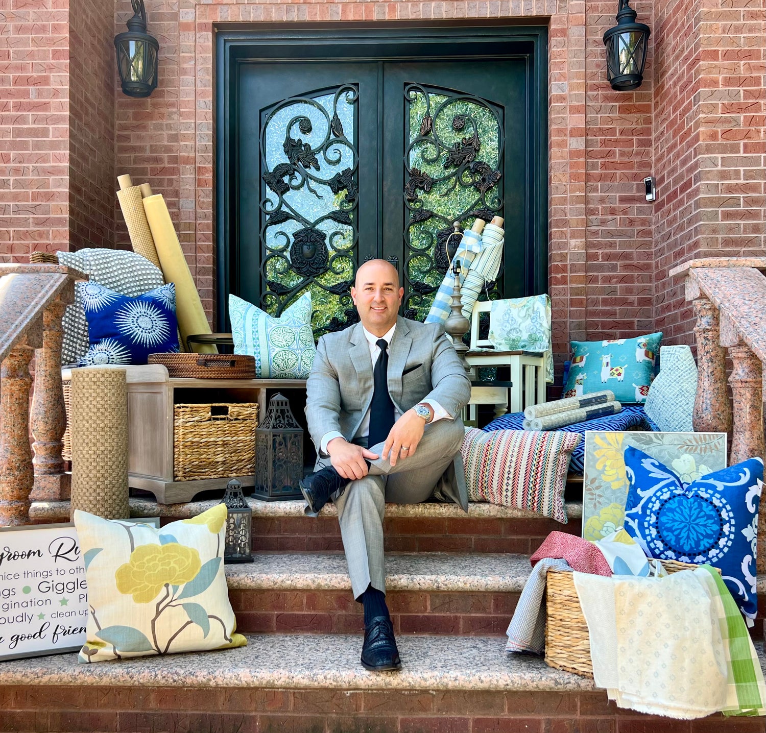 Elegant outdoor decor scene featuring colorful throw pillows, woven baskets, fabrics, and a stylish light fixture on brick steps.