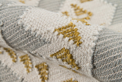 Close-up of a chunky woven rug in ivory, pale gray and mustard yellow with a textured geometric pattern
