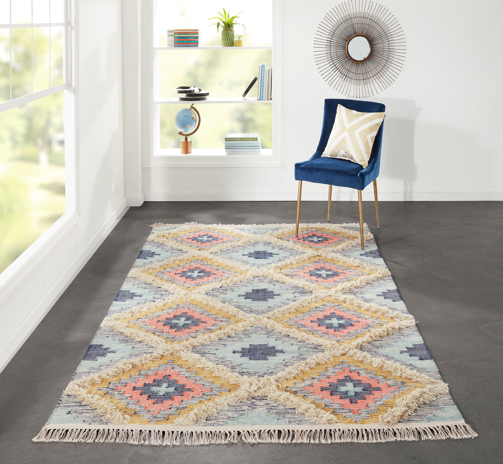 Pastel geometric kilim rug with fringe in an airy living room; blue velvet chair with gold legs beside a sunburst mirror.