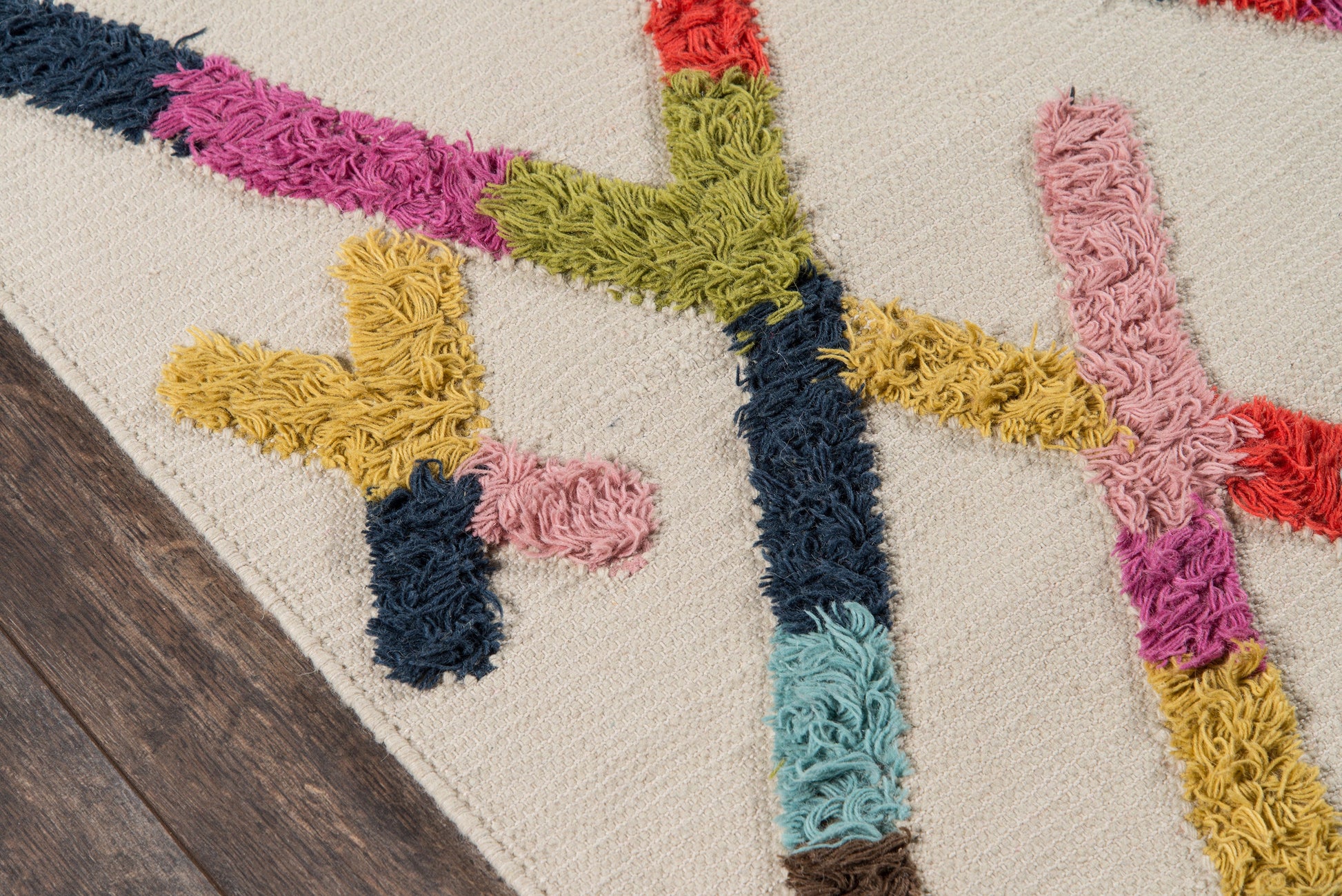 Beige tufted rug with bold multicolor shag lines in pink, teal, navy, yellow, green, and red on a wood floor.