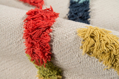 Beige textured woven runner with chunky multicolor fringe tassels in red, yellow, green and blue.