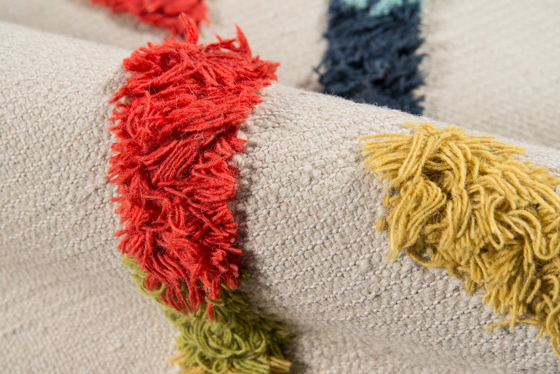 Beige textured woven rug with fluffy multi-color fringe tassels in red, yellow, green & navy.