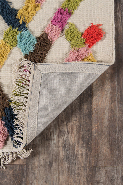 Beige rug with multicolor shaggy fringe geometric pattern; curled corner reveals light gray woven backing on wood floor.