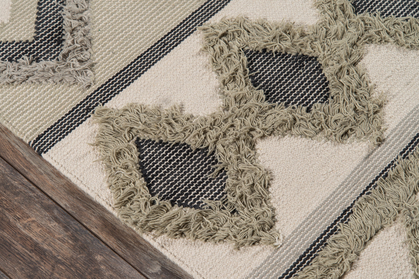 Beige woven rug with navy stripes and olive shag fringe forming star-like frames on a wooden floor.