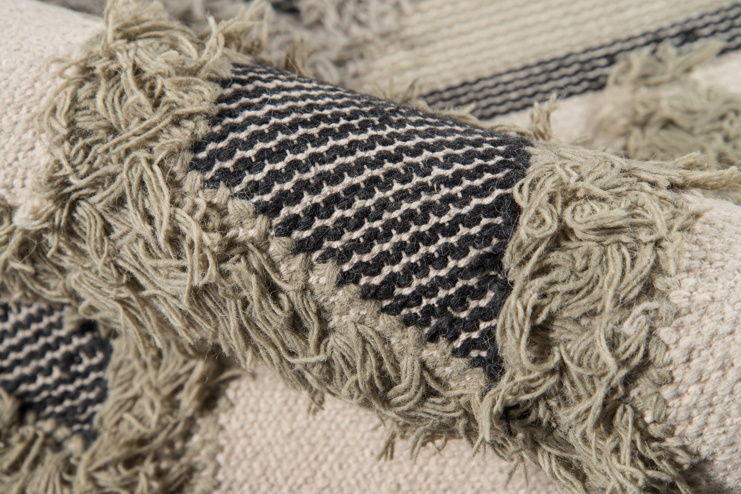 Beige woven rug with a black and cream striped band and shaggy fringe along edges.
