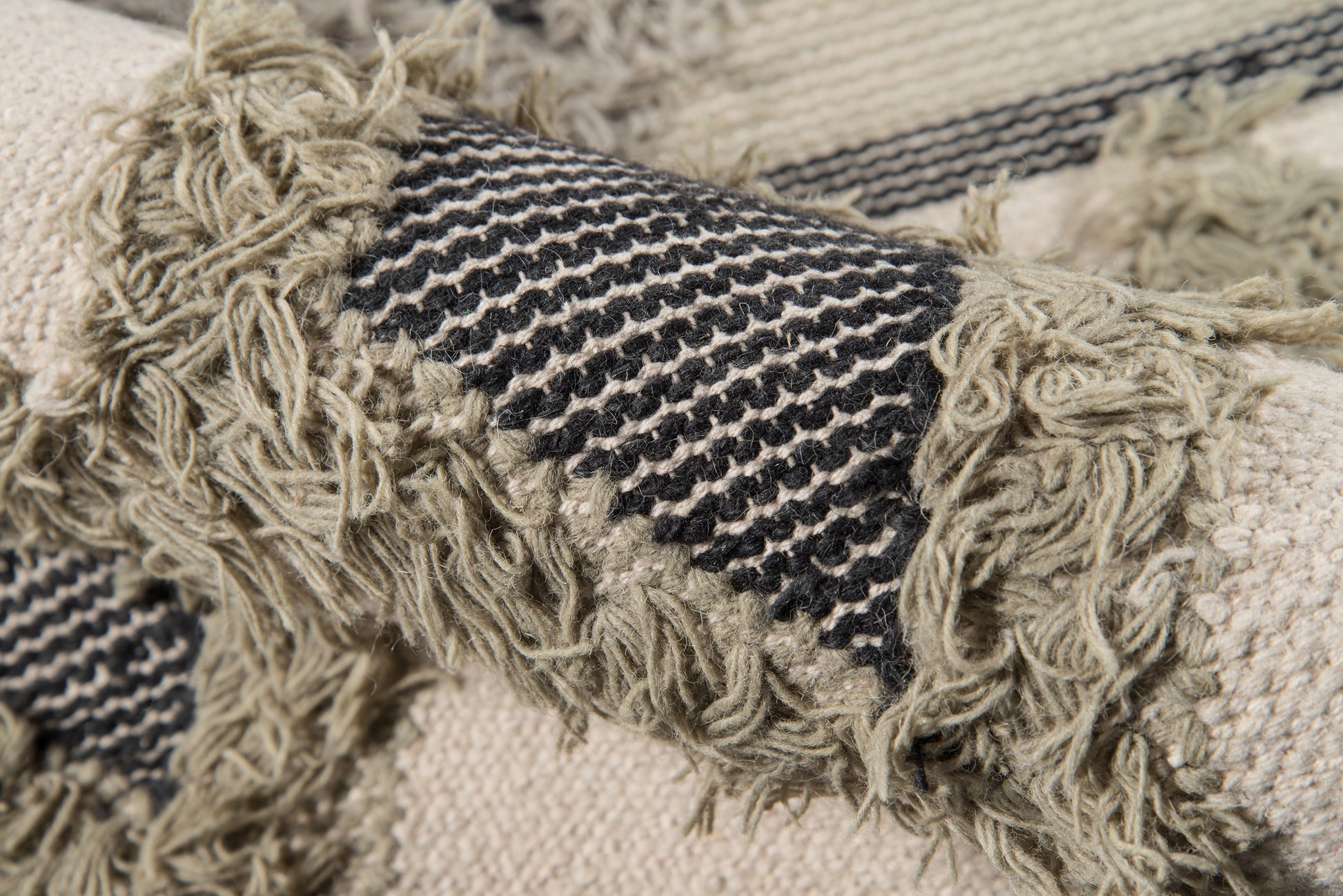 Beige woven rug with black striped band and chunky fringe tassels; textured boho style.